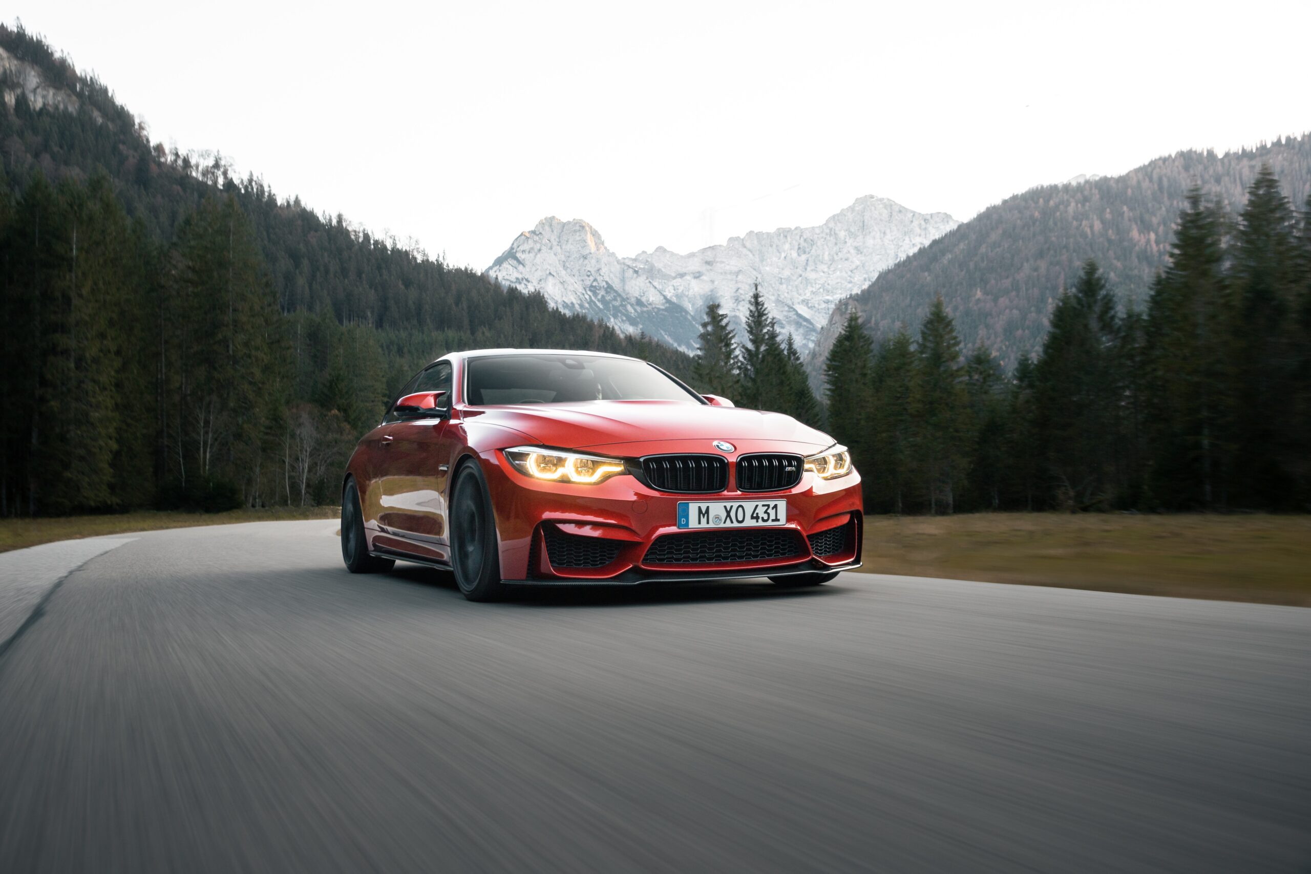 a red car on a road with trees and mountains in the background