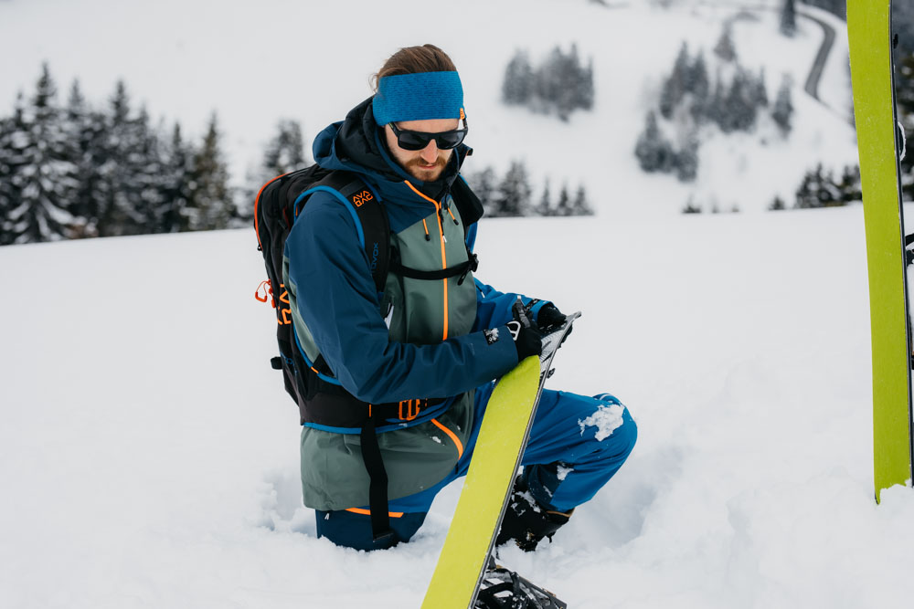 a man kneeling in the snow holding a splitboard