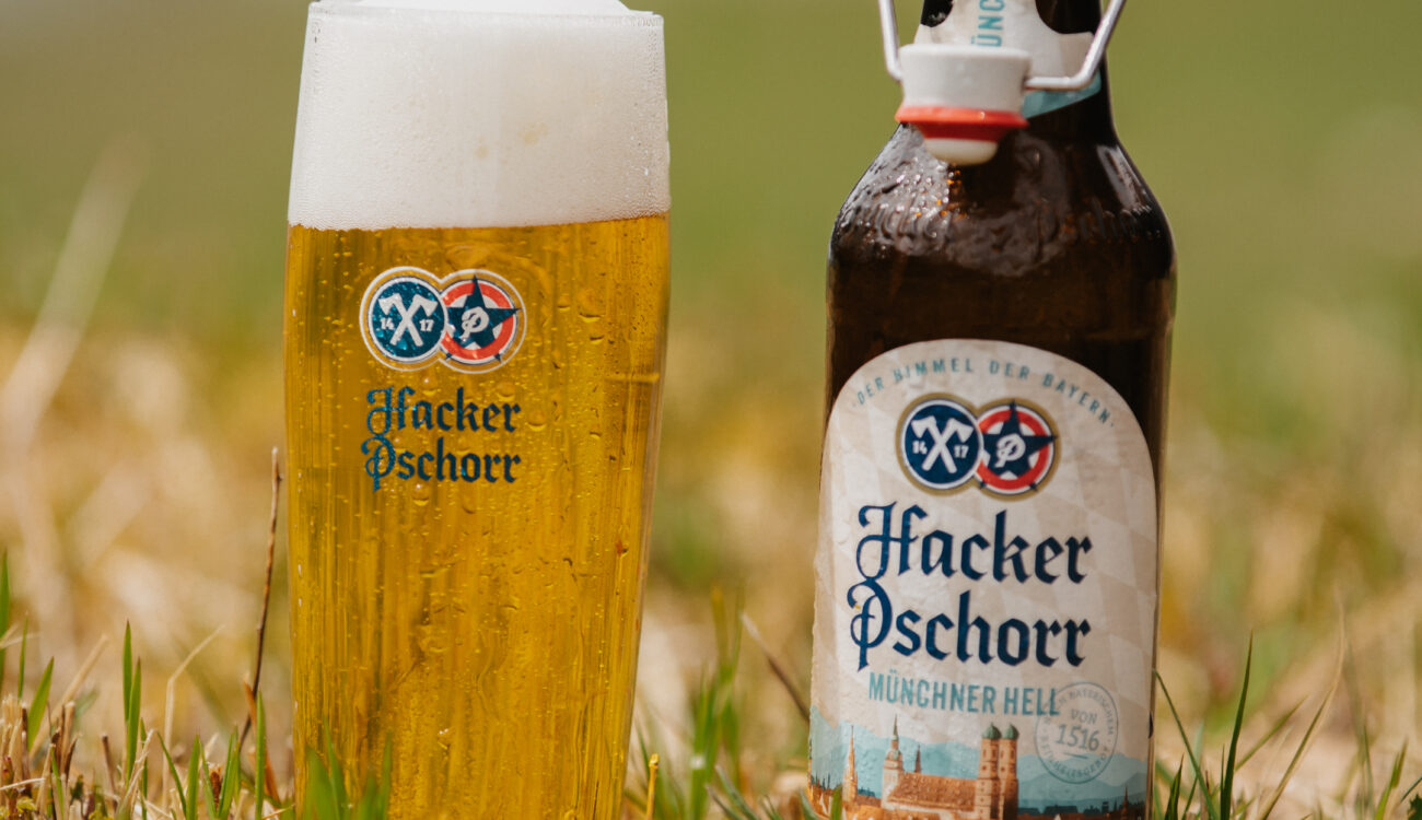 a bottle and glass of Hacker Pschorr beer in the grass